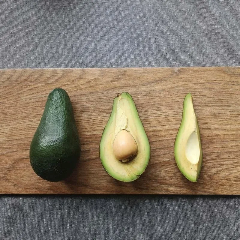 Whole, halved and sliced avocado in a row on a wooden board