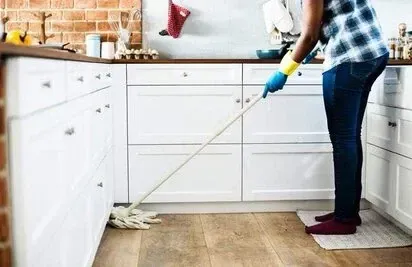 Someone mopping the wooden floor of a white fitted kitchen