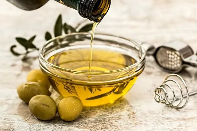 Huile d'olive versée dans un bol en verre, avec des olives vertes