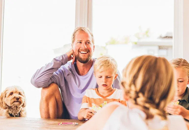 A laughing man at a table with three young children and a small fluffy dog