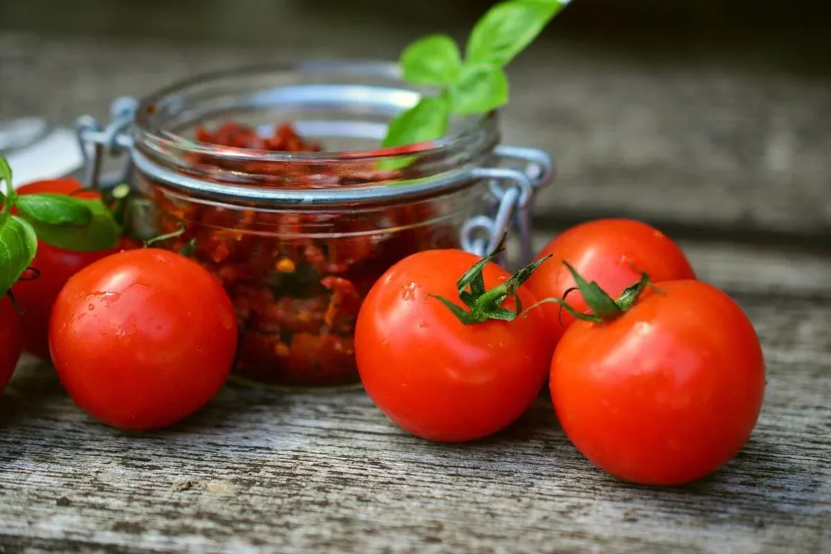 Fresh red tomatoes and a jar of chopped tomato mix on a wooden table